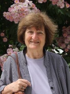 Headshot of June Factor, an older Caucasian woman with short brown hair against a floral backdrop.